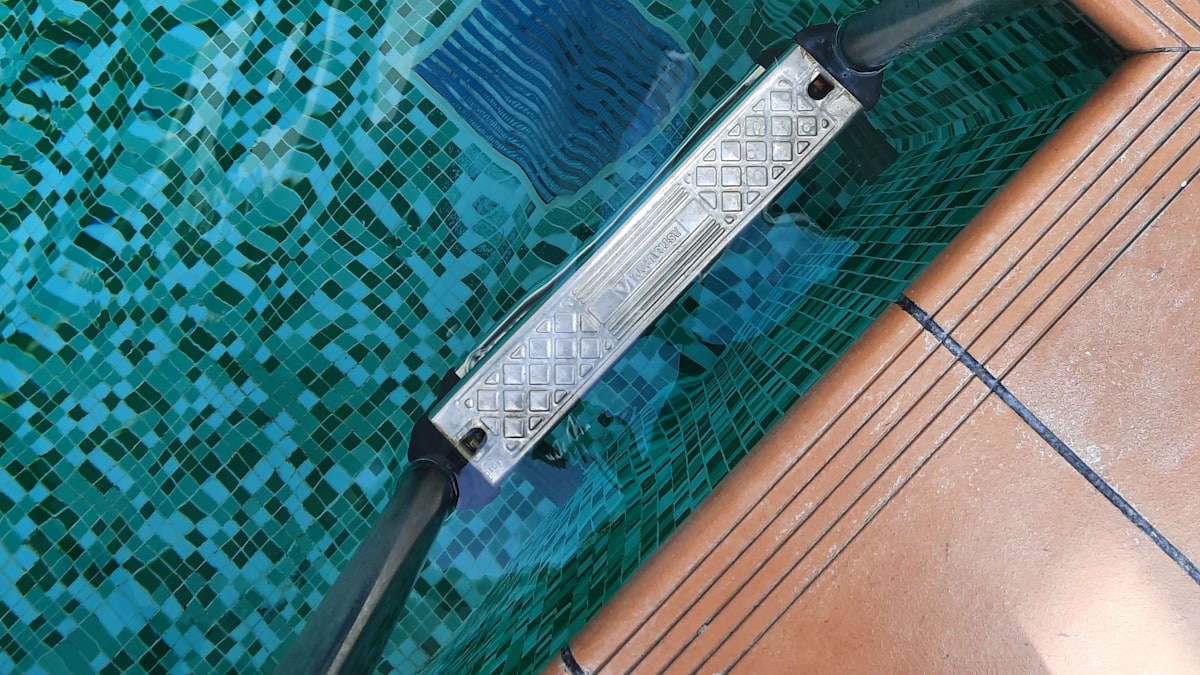Escova de limpeza sobre a borda de uma piscina revestida em pastilhas